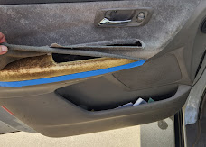 Car door panel with fabric trim partially detached exposing the foam backing before an interior repair