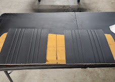 Pair of black vinyl bench seat covers with vertical channel stitching laid out on the upholstery shop table