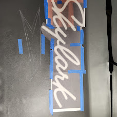 Skylark lettering taped and aligned on black leather during embroidery layout and prep work